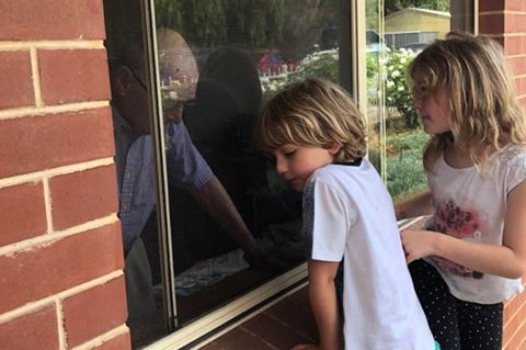 Two children look through the window at an old man inside