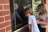 Two children look through the window at an old man inside