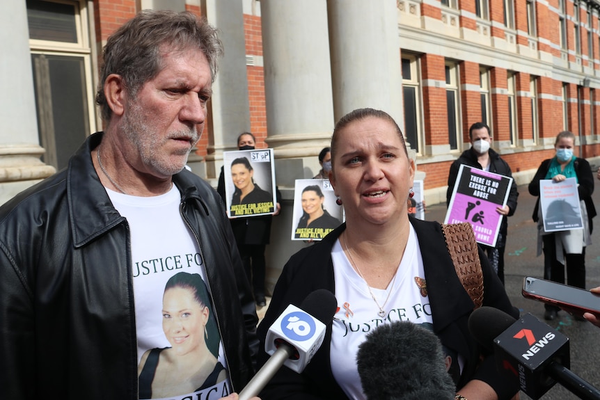 A man and a woman speak to reporters outside court with supporters holding posters behind them.