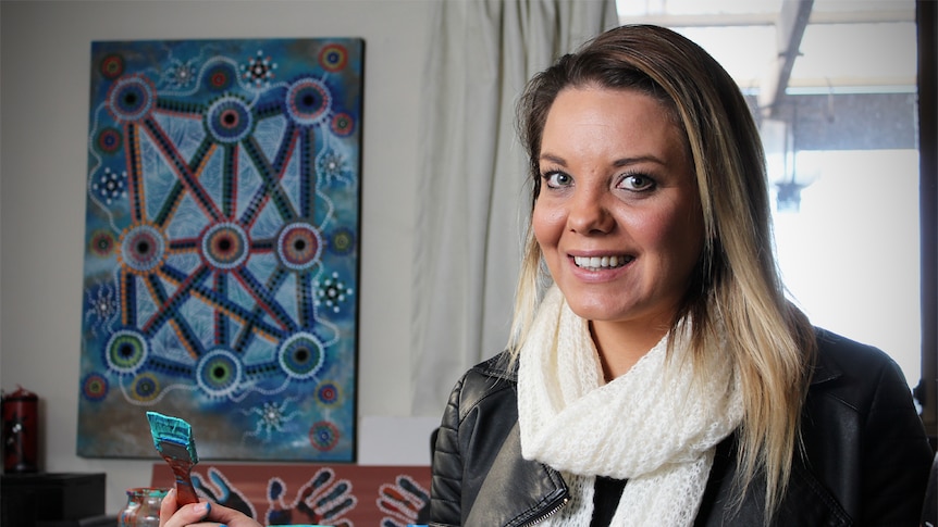 Lani Balzan sits holding a paint brush.