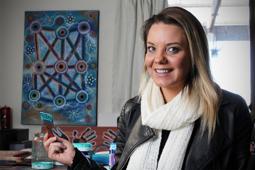 Lani Balzan sits holding a paint brush.