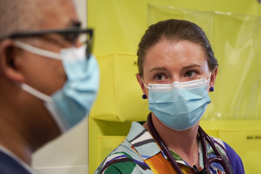 A female doctor wearing a mask looks over at a male doctor