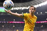 A male soccer player wearing yellow holds out his hand for a ball in a stadium