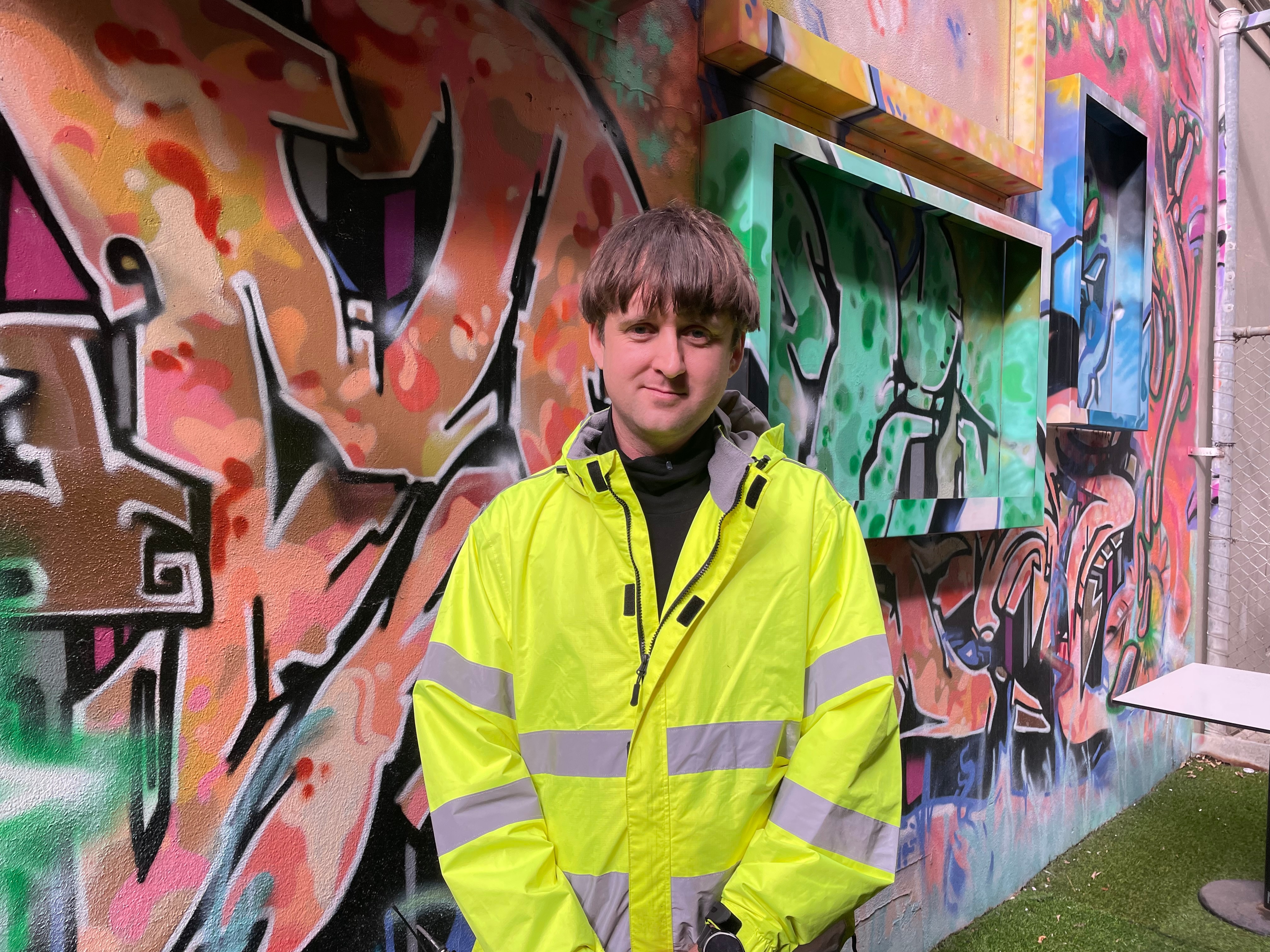 Young delivery driver wearing high visibility vest with graffiti wall in background