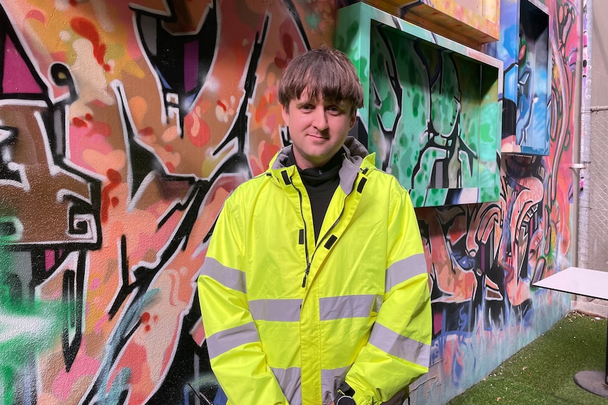 Young delivery driver wearing high visibility vest with graffiti wall in background