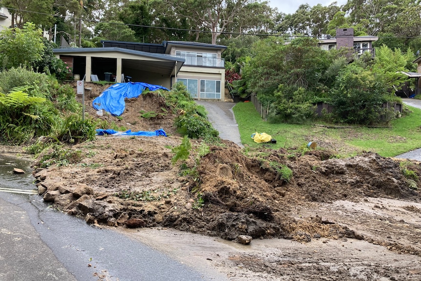 A mass of dirt and rubble spills onto the road in front of a house