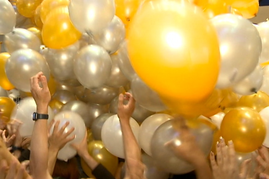 A bunch of yellow balloons with people reaching up for them.