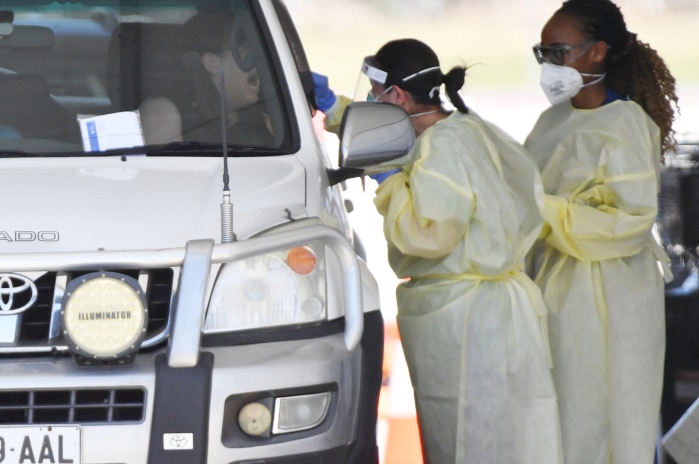 Two women wearing protective equipment, talking to a car passenger at a COVID testing drive-through.