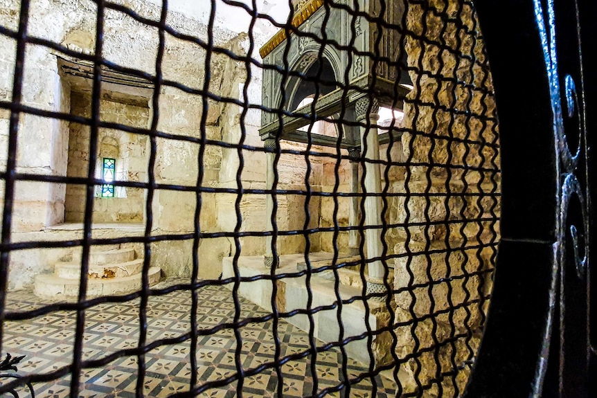 A small room with wall made of stone and closed by a wired gate