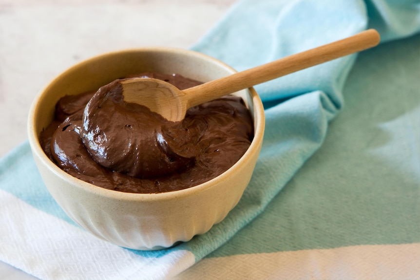 A bowl of chocolate mousse on a table, wooden spoon still in the bowl, it can be made with avocado.