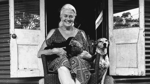 Julie O'Shea sits her front steps with two chooks on her lap and her dog by her side