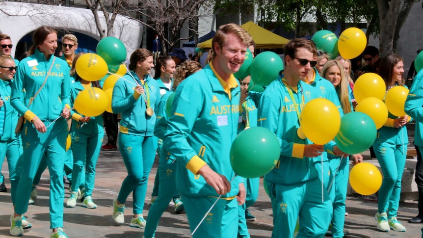 Olympians in their green and gold tracksuits carry green and gold balloons.