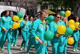 Olympians in their green and gold tracksuits carry green and gold balloons.