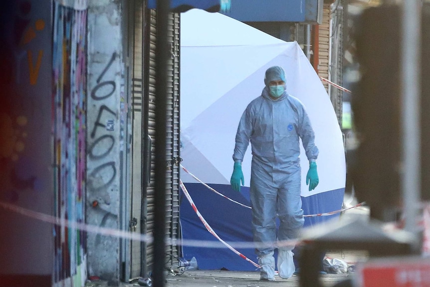 A man in a disposable suit, wearing a a face mask and disposable glvoes walks away from a tent set up on the street