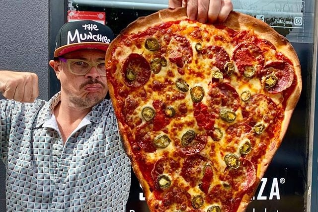 A man making a fist with one hand and holding a huge pizza in another