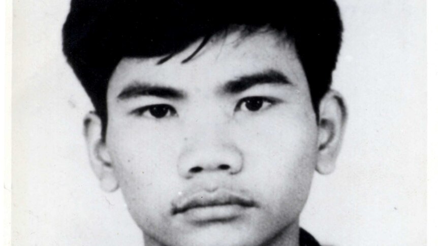 A black and white photo of a young Cambodian man staring straight at the camera. He is wearing black and has a number on shirt.