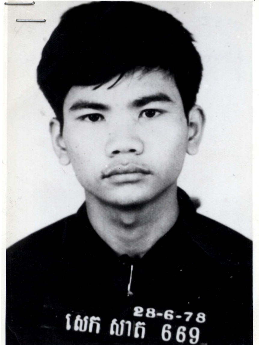 A black and white photo of a young Cambodian man staring straight at the camera. He is wearing black and has a number on shirt.