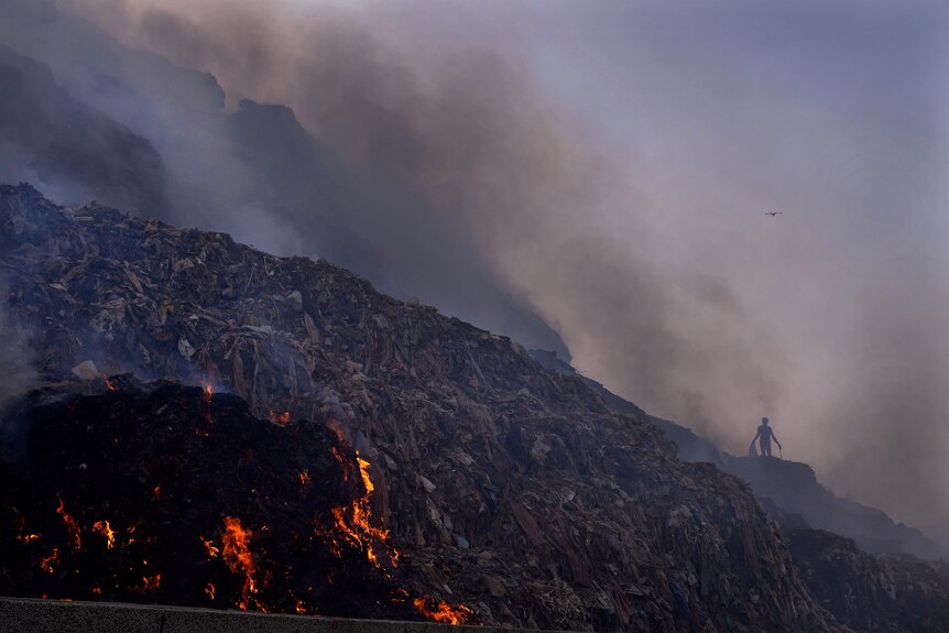 A ragpicker looks for reusable items while a fire rages at the Bhalswa landfill