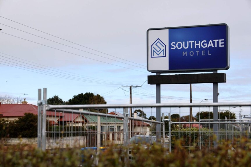 An elevated blue sign with the words 'Southgate Motel' stands above a wall of scaffolding.
