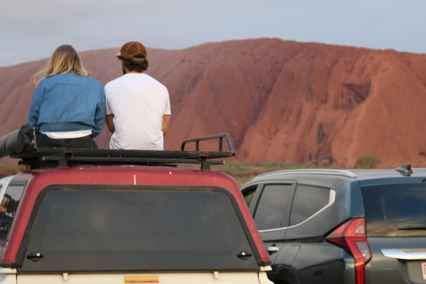 Tourists look out over the rock in a largely deserted carpark.