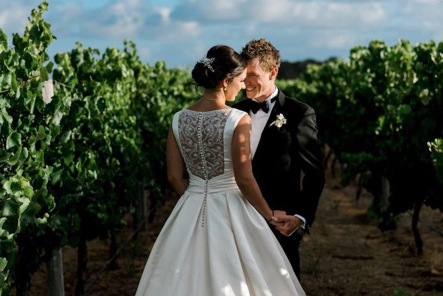 A bride and groom pose between grape vines
