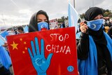 A woman in a headscarf holds a placard reading 'stop China'