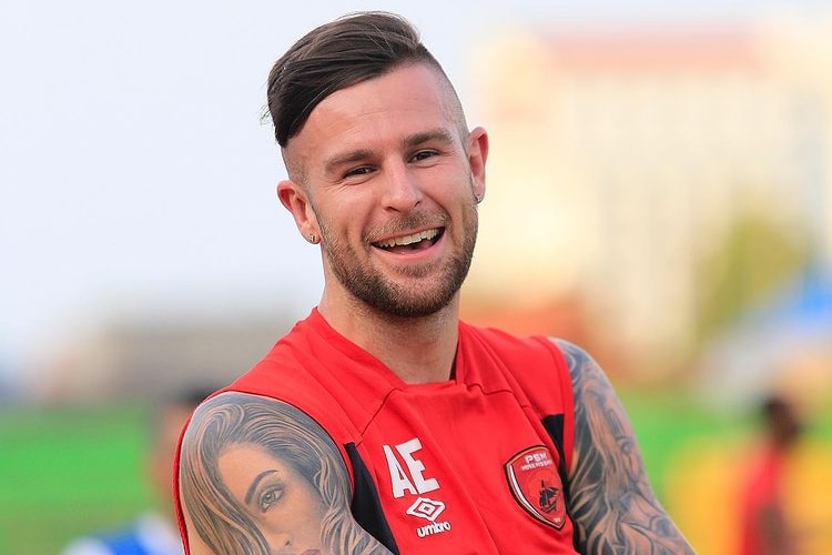 A man in a singlet with tattoos smiles at the camera