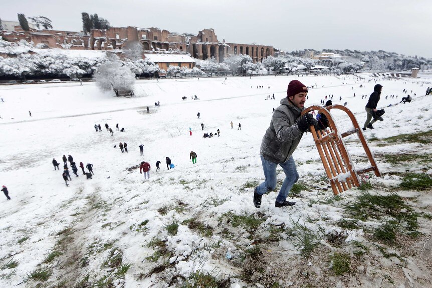 A man carries a sled during a heavy snowfall, at the Circus Maximus, in Rome.