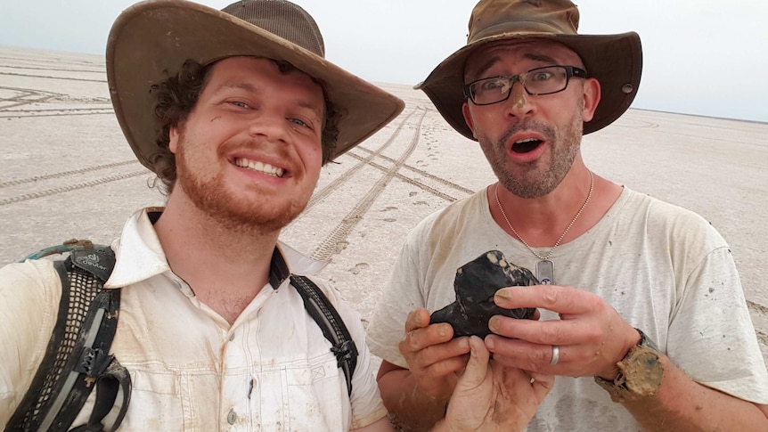Robert Howie and Phil Bland from Curtin University hold a 4.5-billion-year-old meteorite while standing on Lake Eyre.