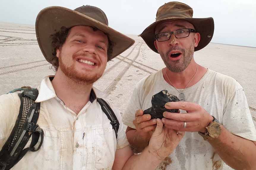 Robert Howie and Phil Bland from Curtin University hold a 4.5-billion-year-old meteorite while standing on Lake Eyre.