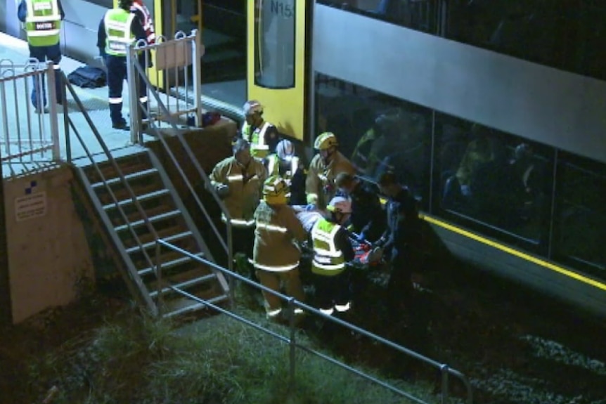 Fire and Rescue officers and police carry a man on a stretcher after rescuing him from under a train