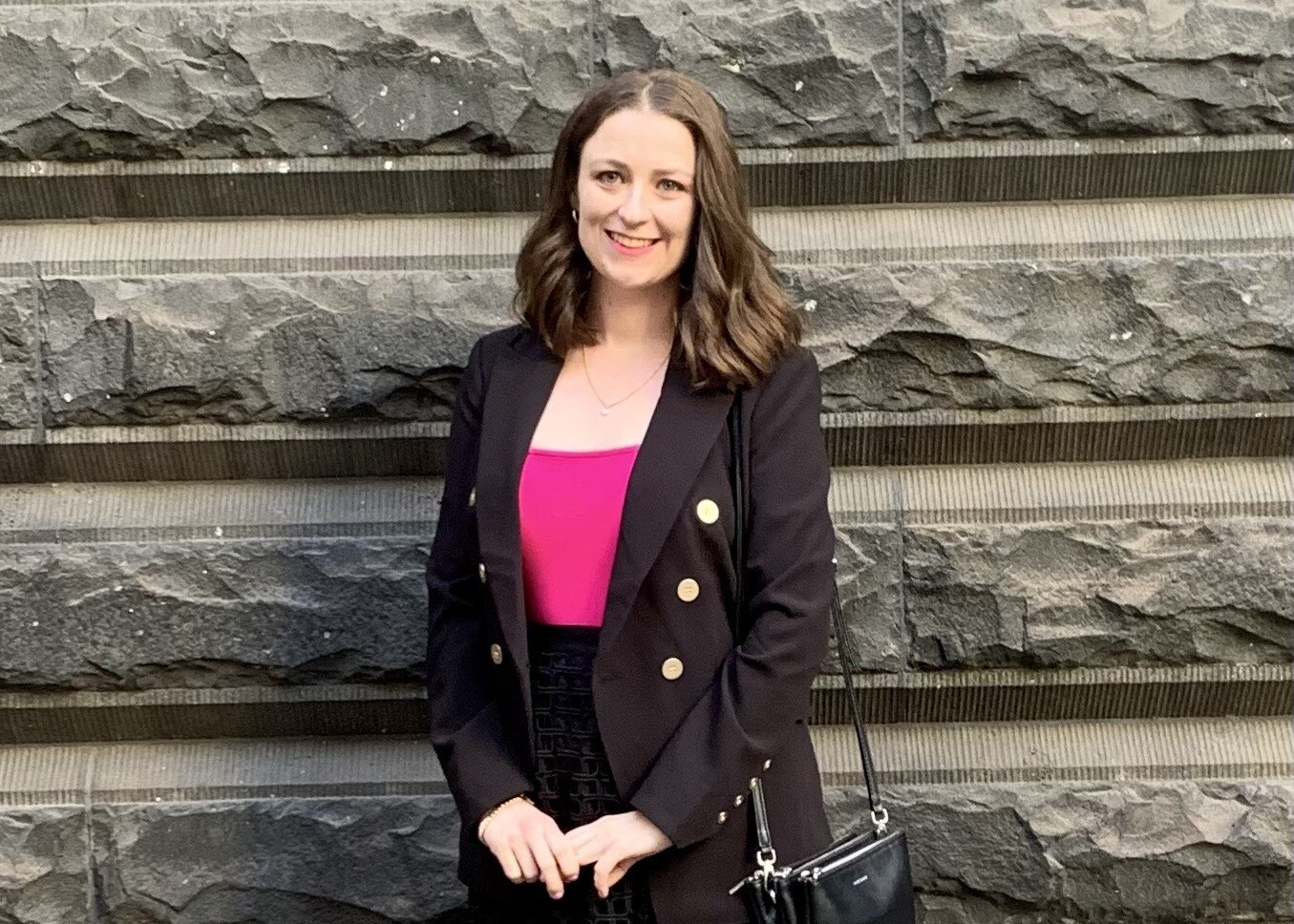 A young woman stands against a stone wall.