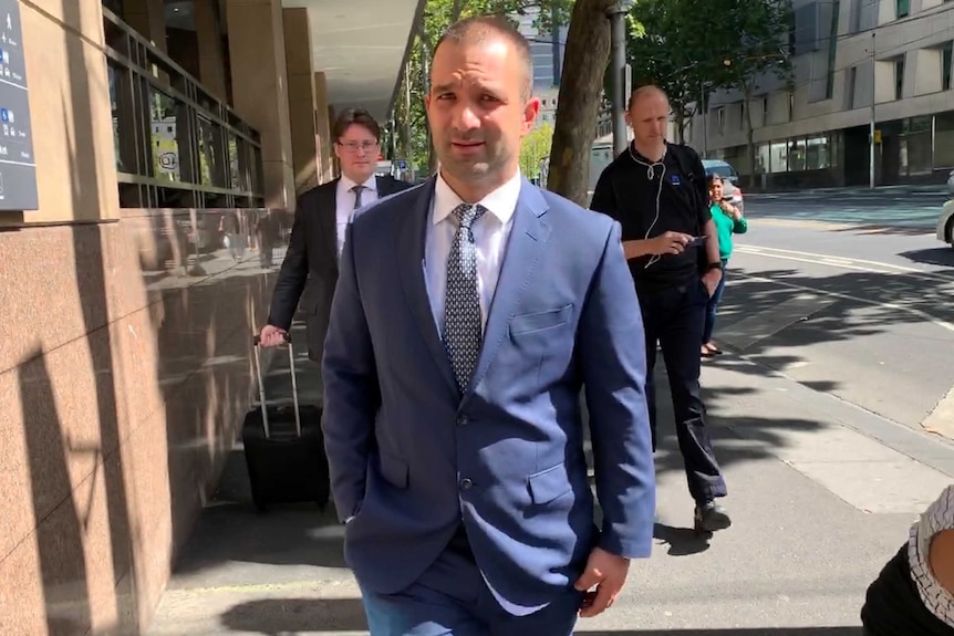 A balding man wearing a blue suit walks away from court.