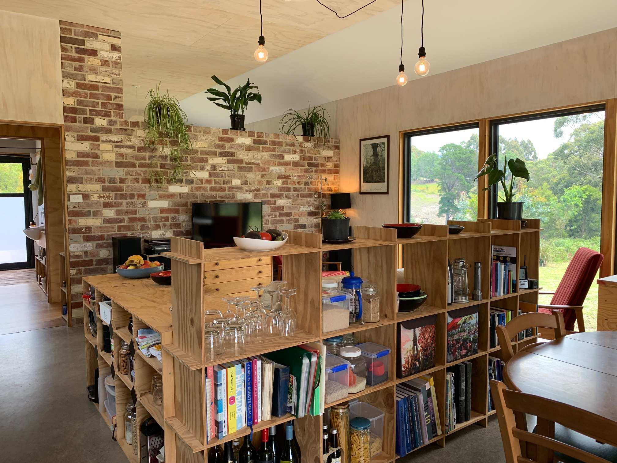 A living room, including hanging lights, a bookshelf, a table and television. It's very "Scandi", so bare wood, brick etc