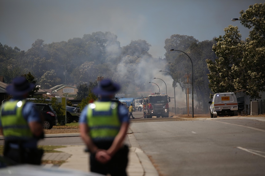 Police stand on a street as smoke rages in the background