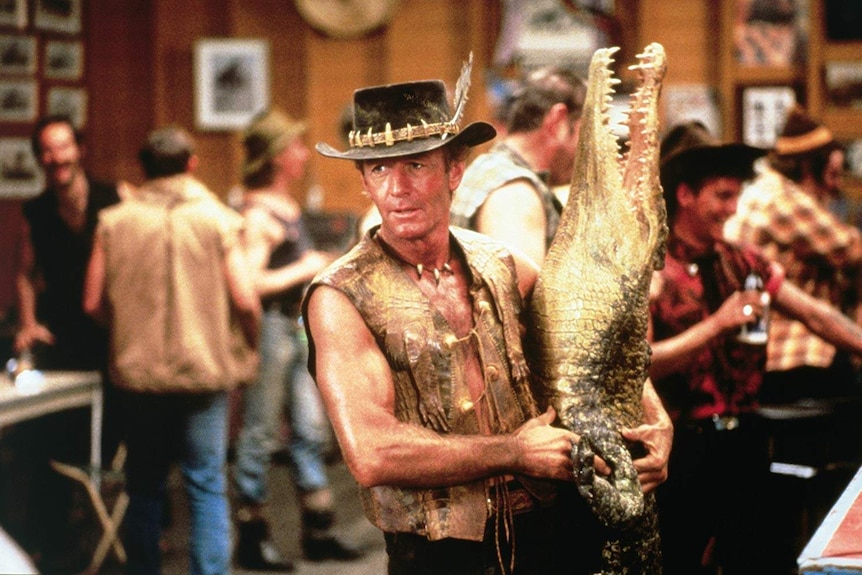 A still from the 1986 film Crocodile Dundee of Paul Hogan holding a crocodile.