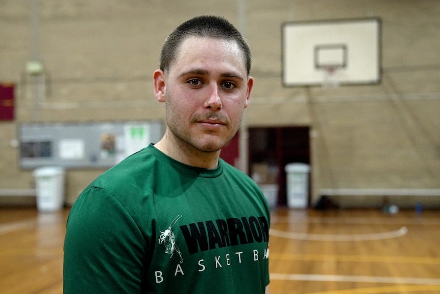 Man wearing green t-shirt standing on a basketball court. 