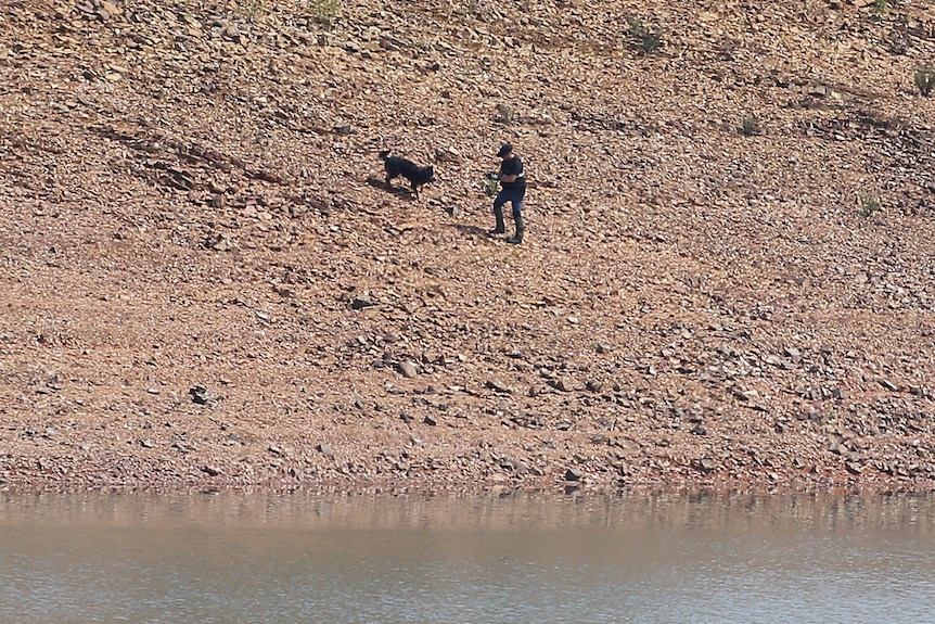 Police officer and dog on bank of dam.