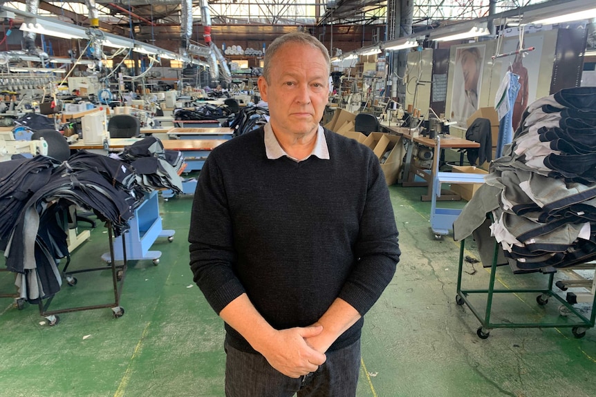 Gary Campbell, wearing a black jumper, stands in a garment factory.