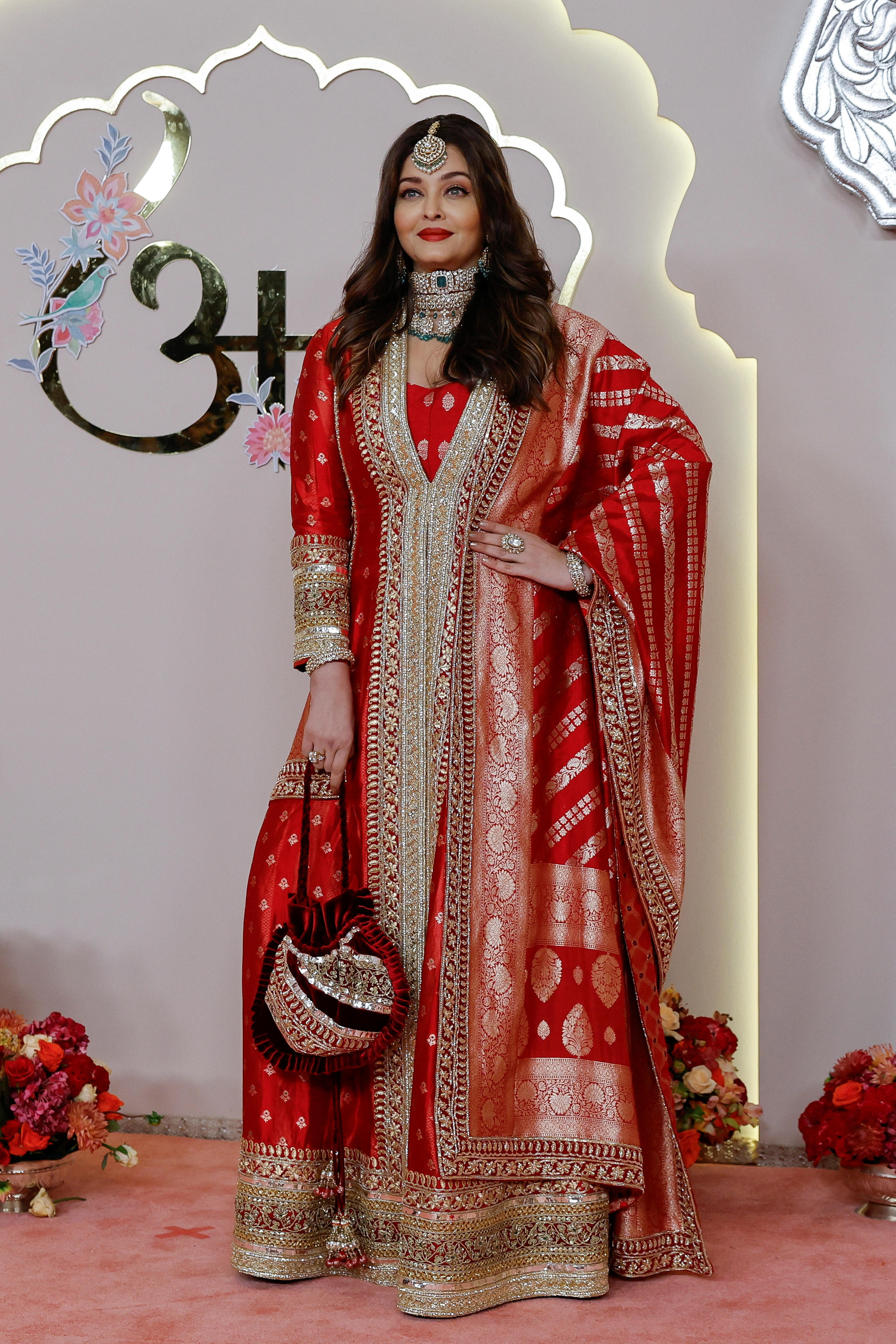 Aishwarya Rai Bachchan wearing a long tunic-like red dress with gold trim and embellishments and flowy sleeves 