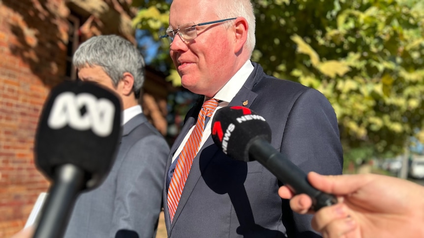 Man walks past news reporters' microphones outside a courthouse.