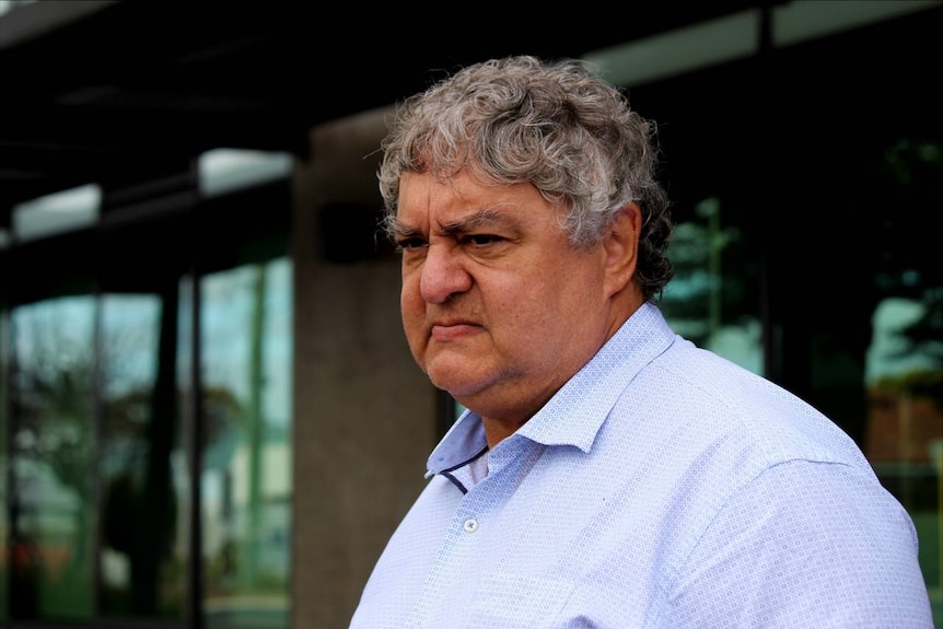 A concerned-looking, grey-haired Aboriginal man in a business shirt.