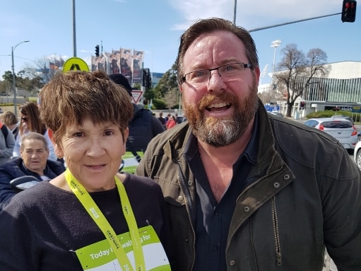 A woman with a medal and a certificate standing with a man with a beard