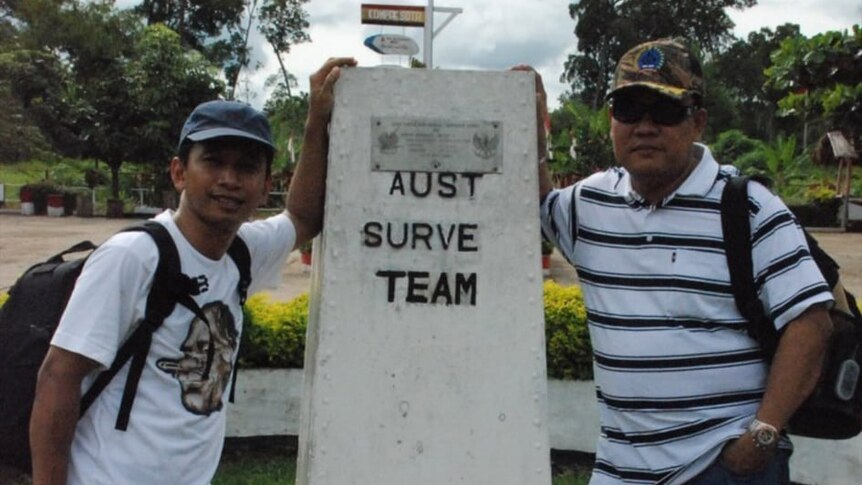 Two men standing with a border sign between Indonesia and PNG