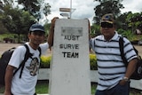 Two men standing with a border sign between Indonesia and PNG