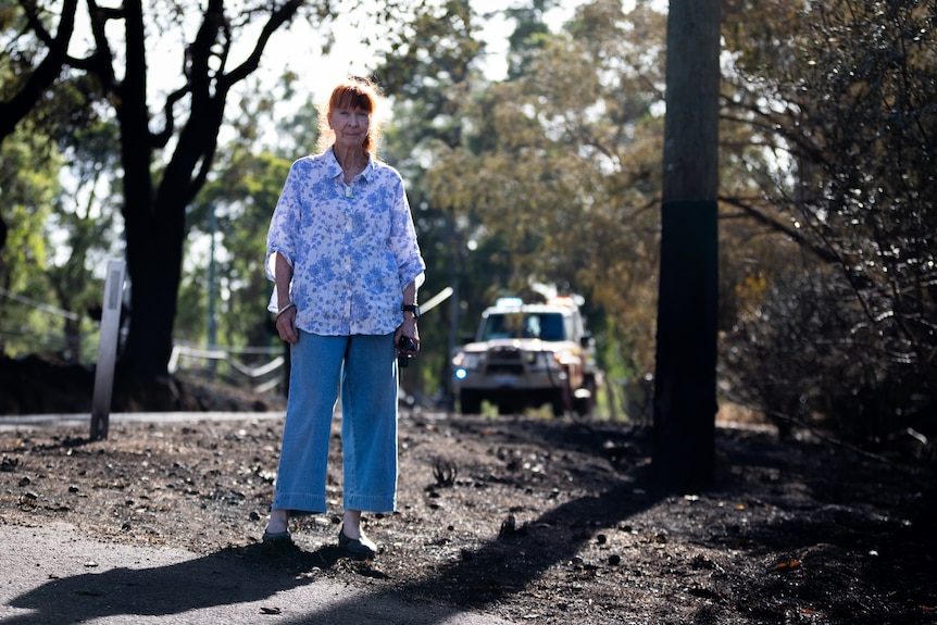 A woman stands on charred bush ground, with a 4WD in the background.