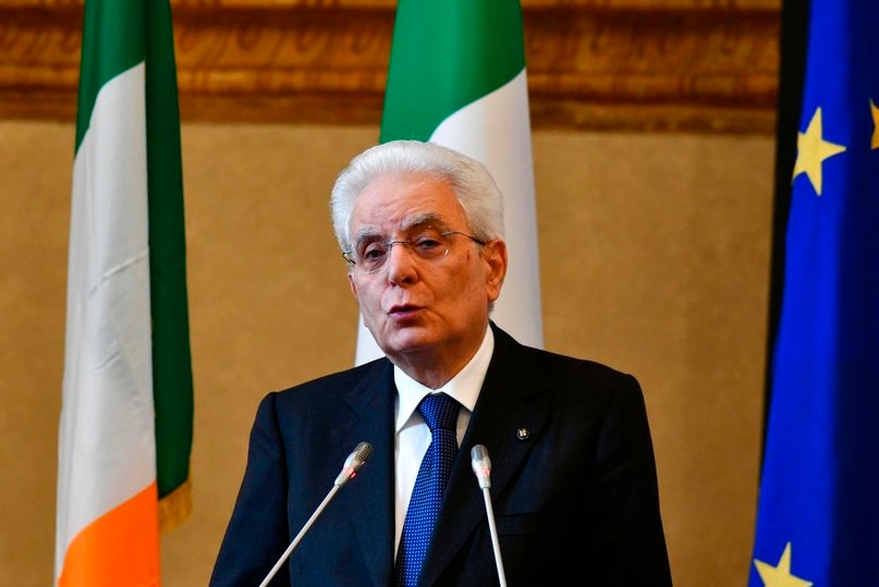 Italian President Sergio Mattarella delivers a speech at a podium with flags behind him