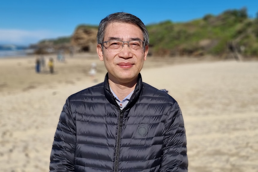 A man on a beach wearing a puffer jacket.