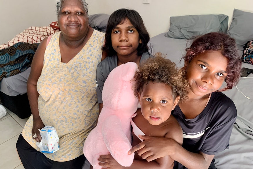 A woman sits on the end of a bed with three children, posing for a photo.