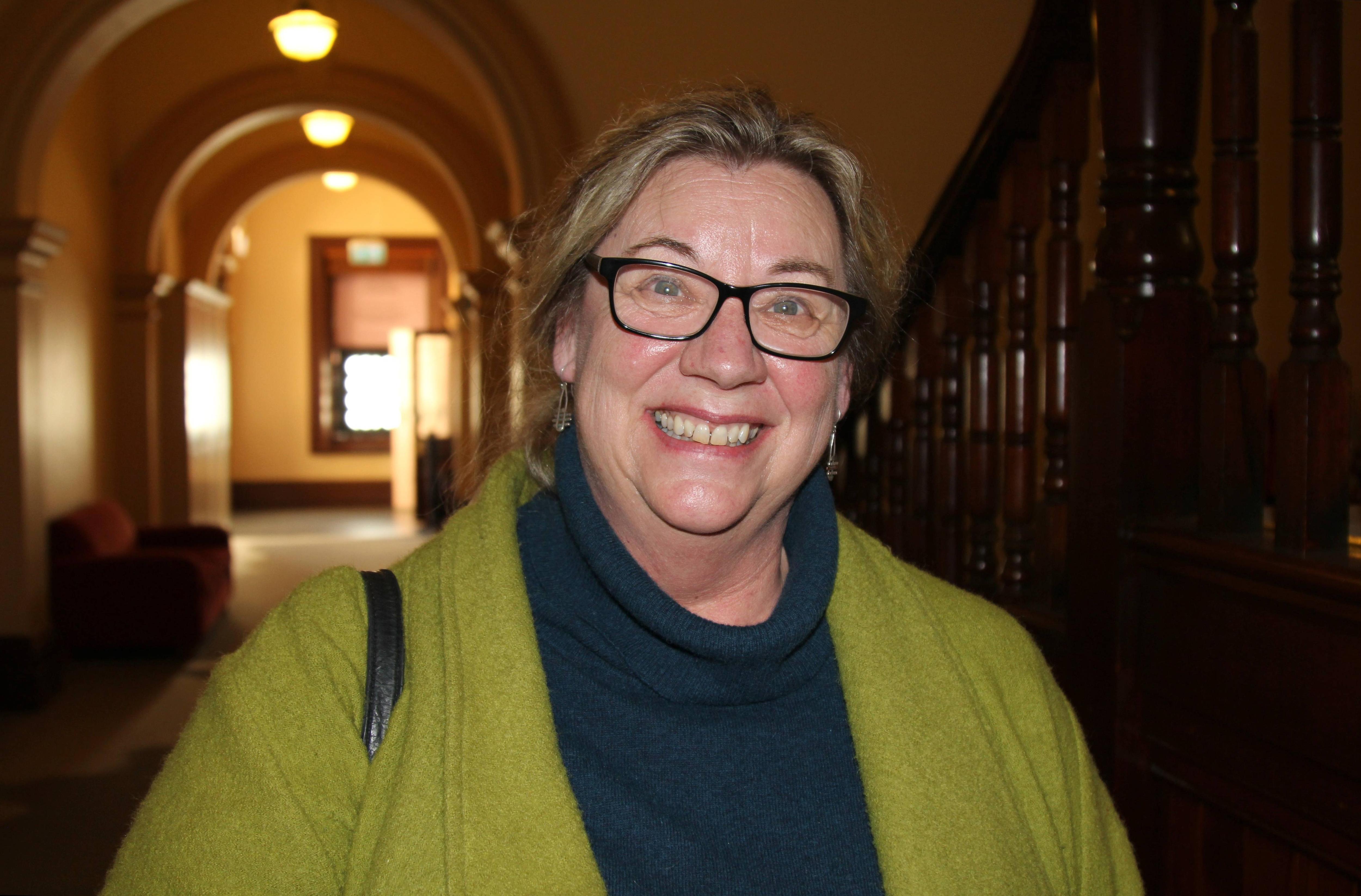 A woman wearing glasses and a green cardigan, smiling.